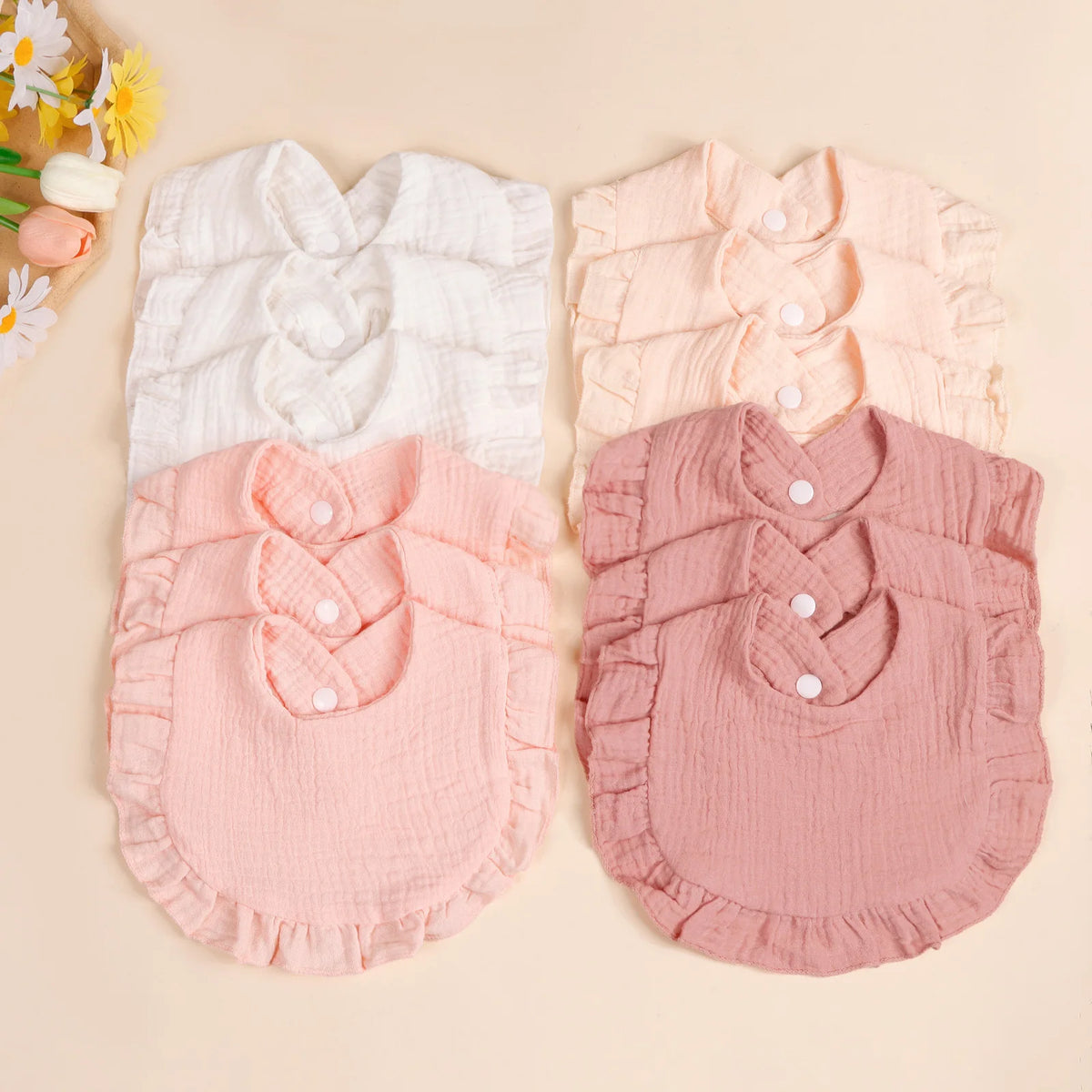 A set of three soft cotton ruffle bibs in white, peach, and dusty rose pink for babies.