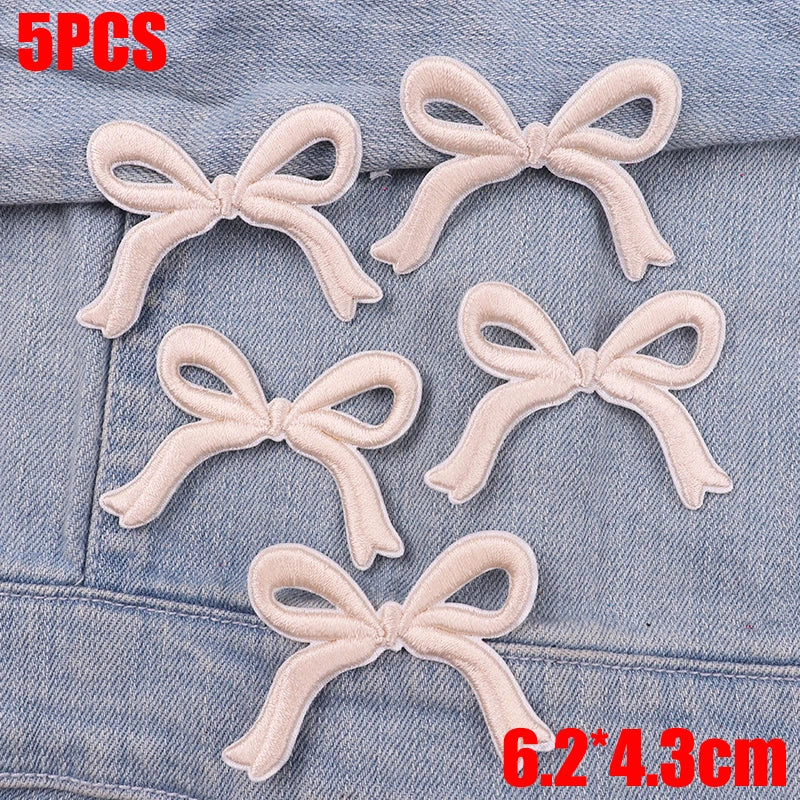 Five light pink embroidered cartoon bow iron-on patches displayed on a denim fabric.