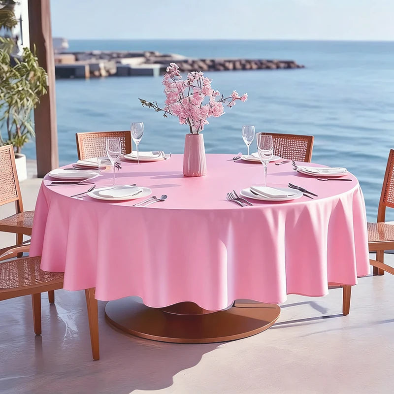A round pink satin tablecloth set for an elegant outdoor dining table with pink flowers and glassware.