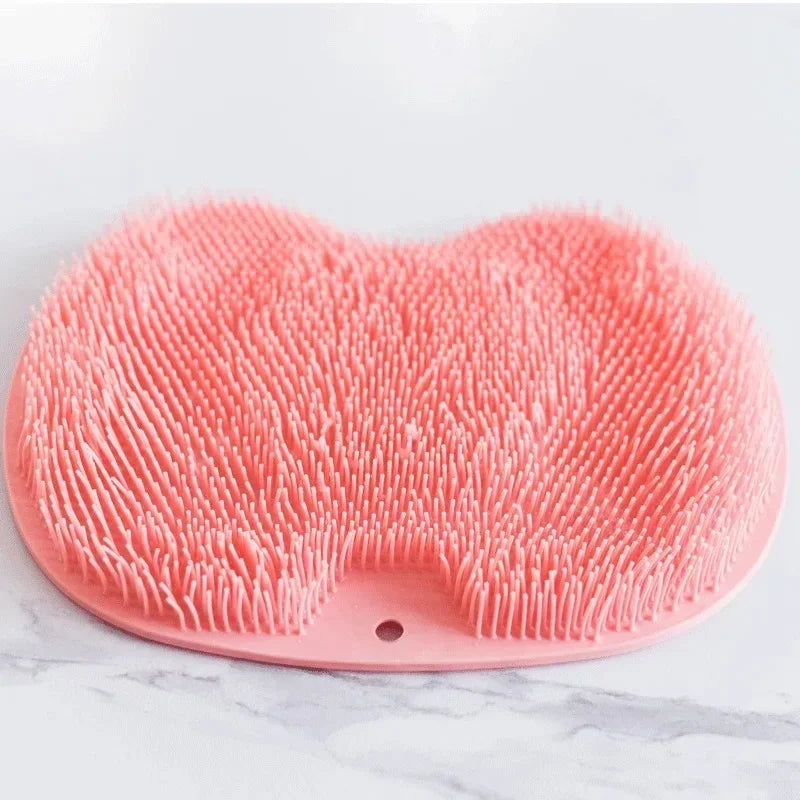 A pink non-slip silicone shower mat with exfoliating bristles resting on a white marble surface.