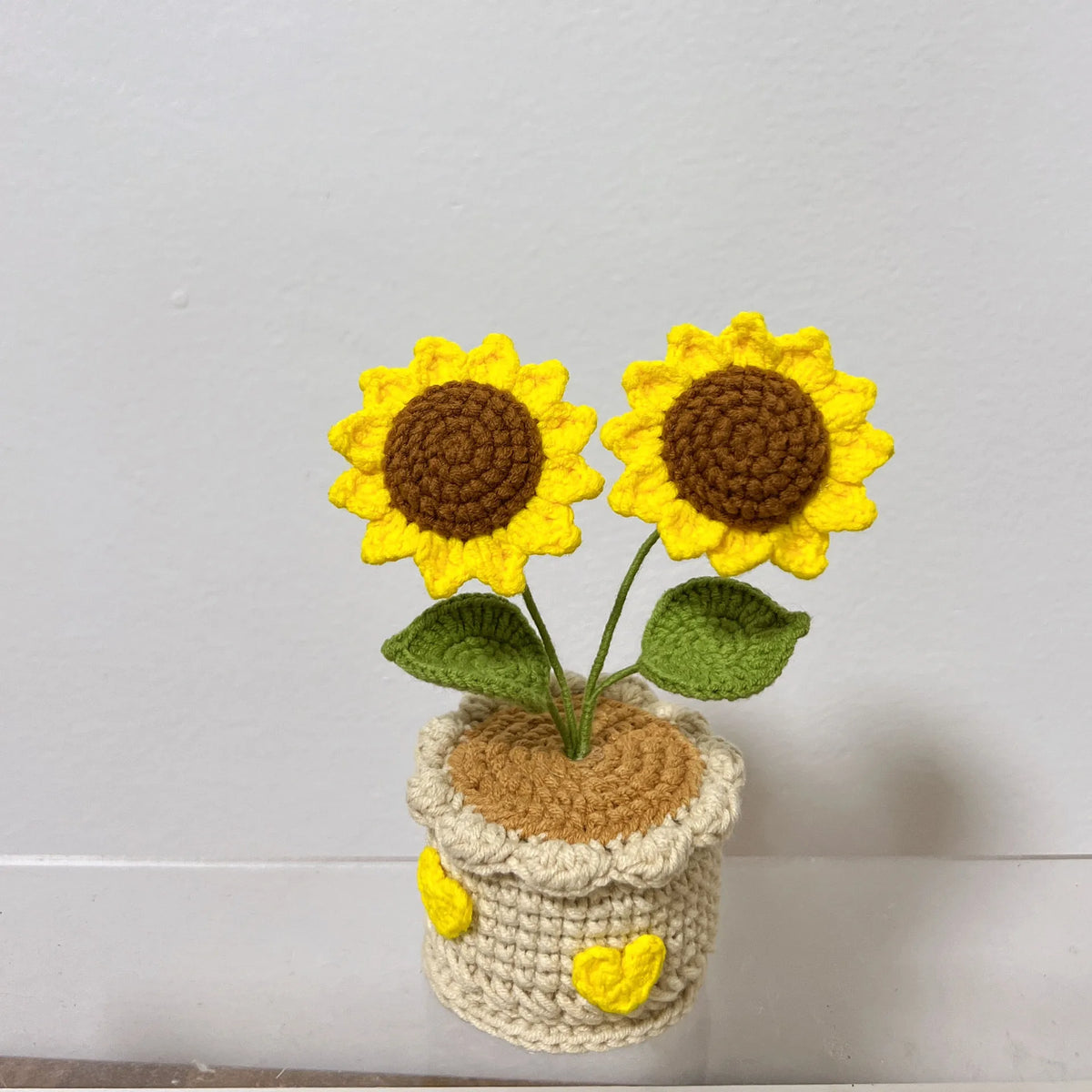 Handcrafted crochet sunflower with green leaves growing out of a beige pot