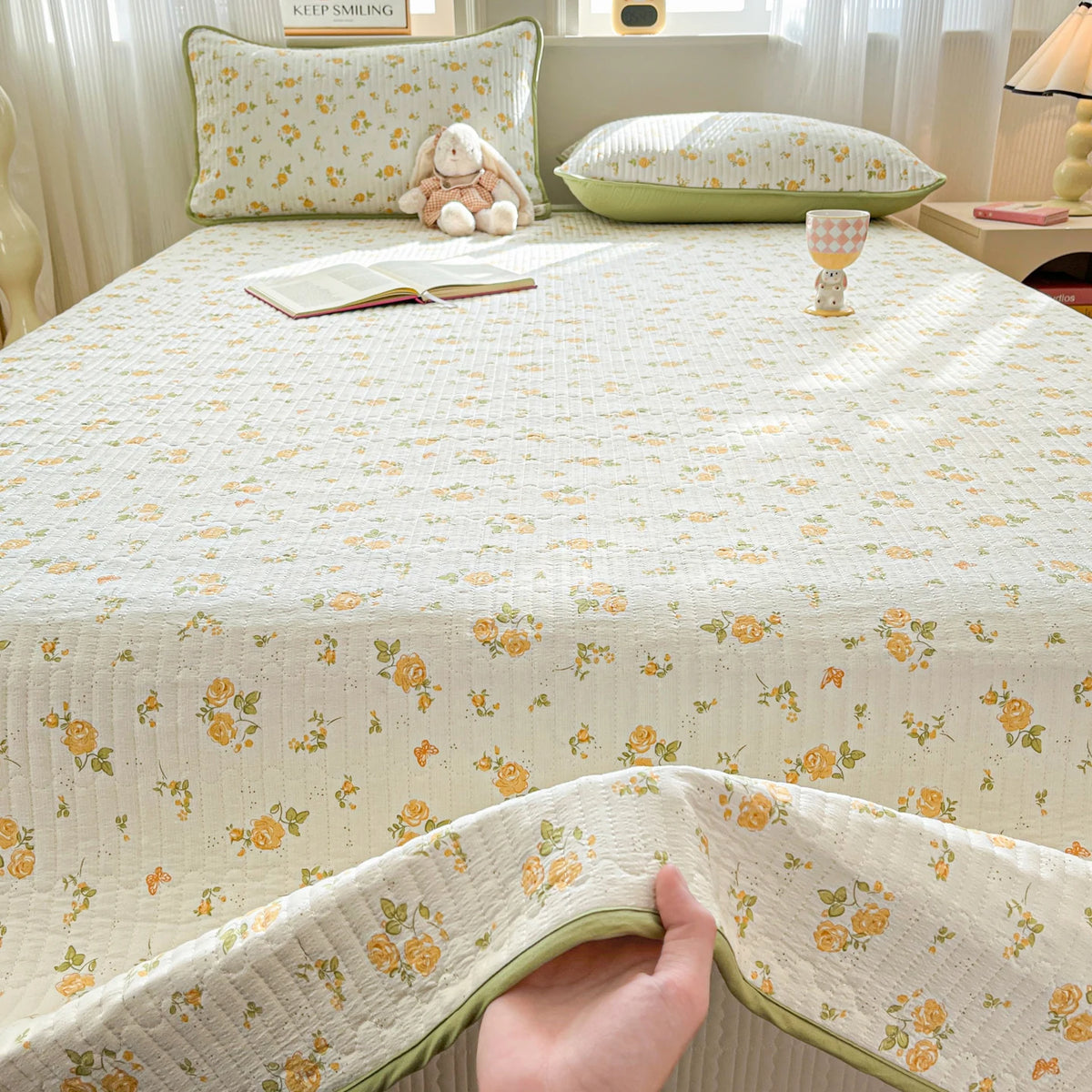 A floral quilted bedspread in cream and yellow tones with a matching dust-proof cover is displayed on a bed.