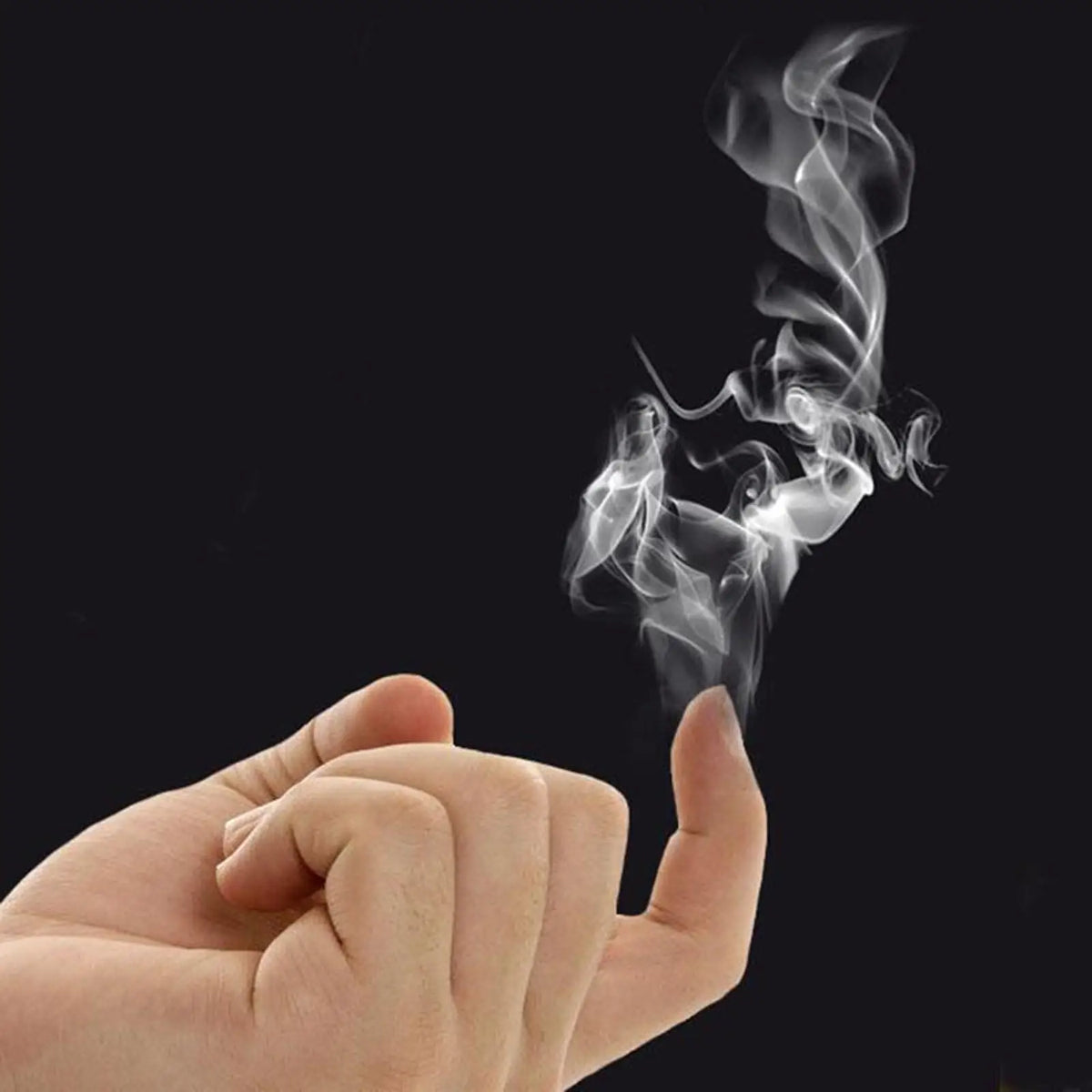 A hand is blowing smoke from a piece of chemical smoke magic paper against a dark background.