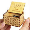 A wooden music box with a lid featuring musical notes and the text Over the Rainbow is held in a hand.