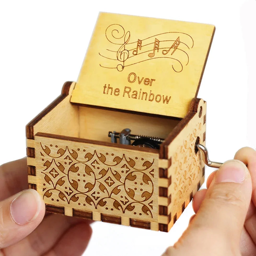 A wooden music box with a lid featuring musical notes and the text Over the Rainbow is held in a hand.