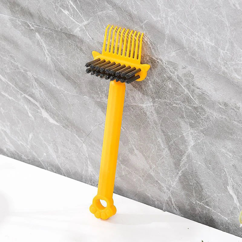 A yellow dual-sided hairbrush cleaner with rake teeth is shown against a gray marble background.