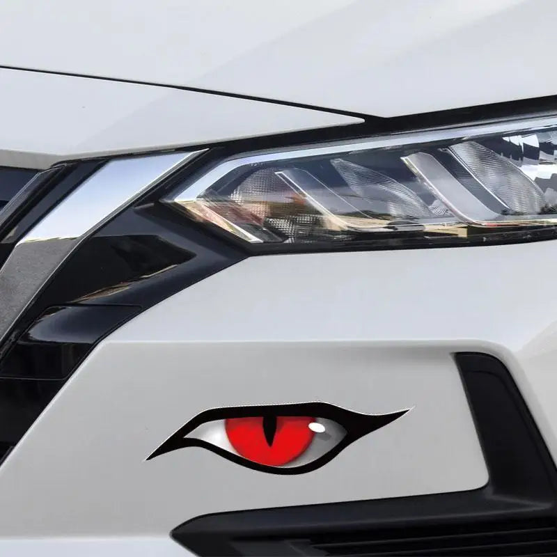 Close-up of a white car headlight with a black cat eye emblem featuring a red iris.