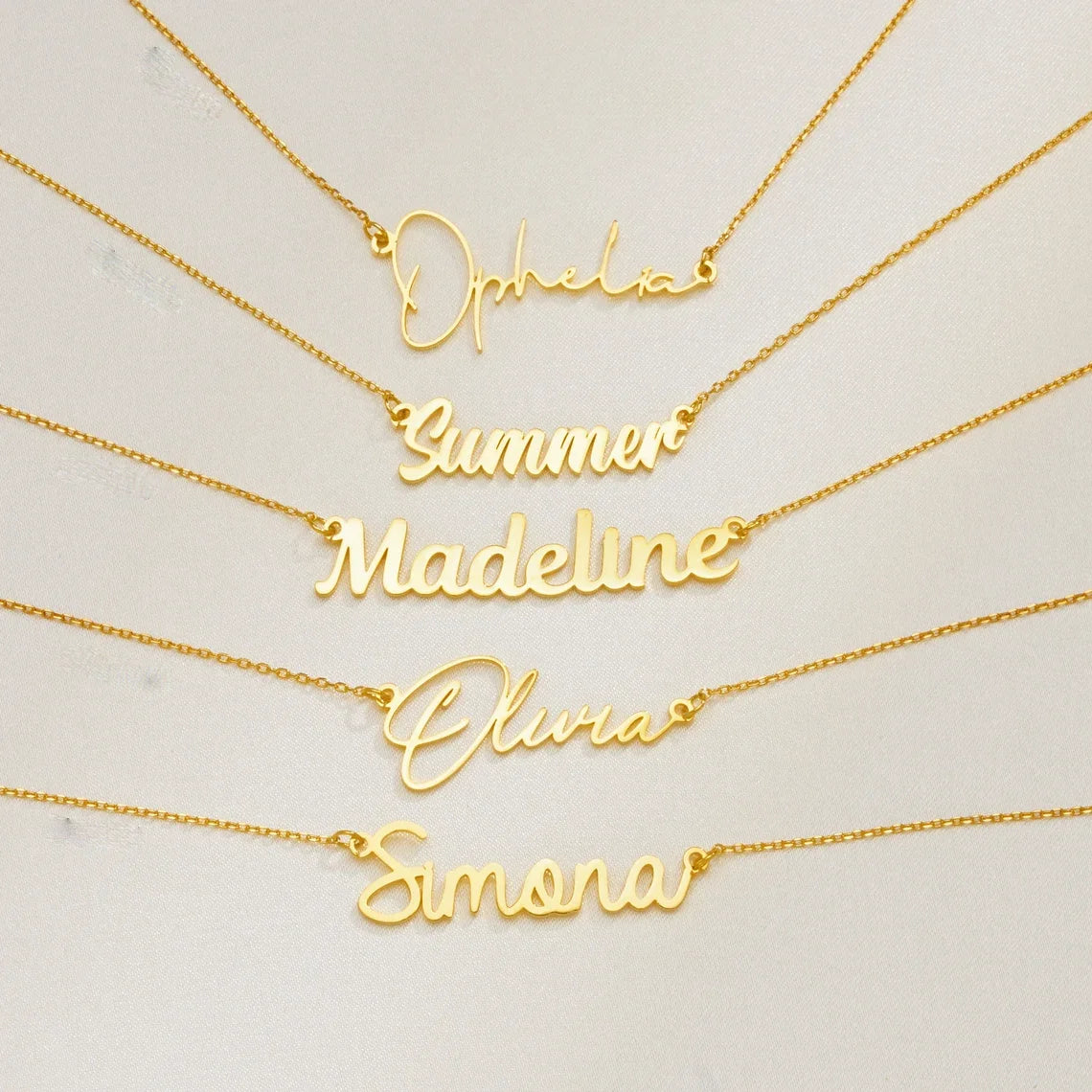 Gold cursive name necklaces featuring names like Ophelia, Summer Madeline, Olivia, and Simona