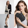 A close-up of a woman holding a black woven clutch bag with a gold chain strap against a light gray background.
