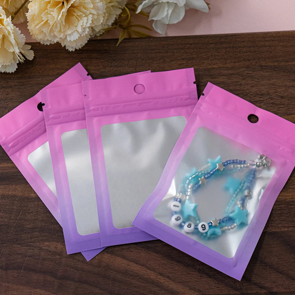 A set of gradient pink and purple resealable zipper pouches with clear windows containing jewelry.
