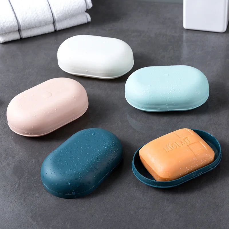 A collection of five white, pink, and blue portable soap containers with lids arranged on a dark gray surface.