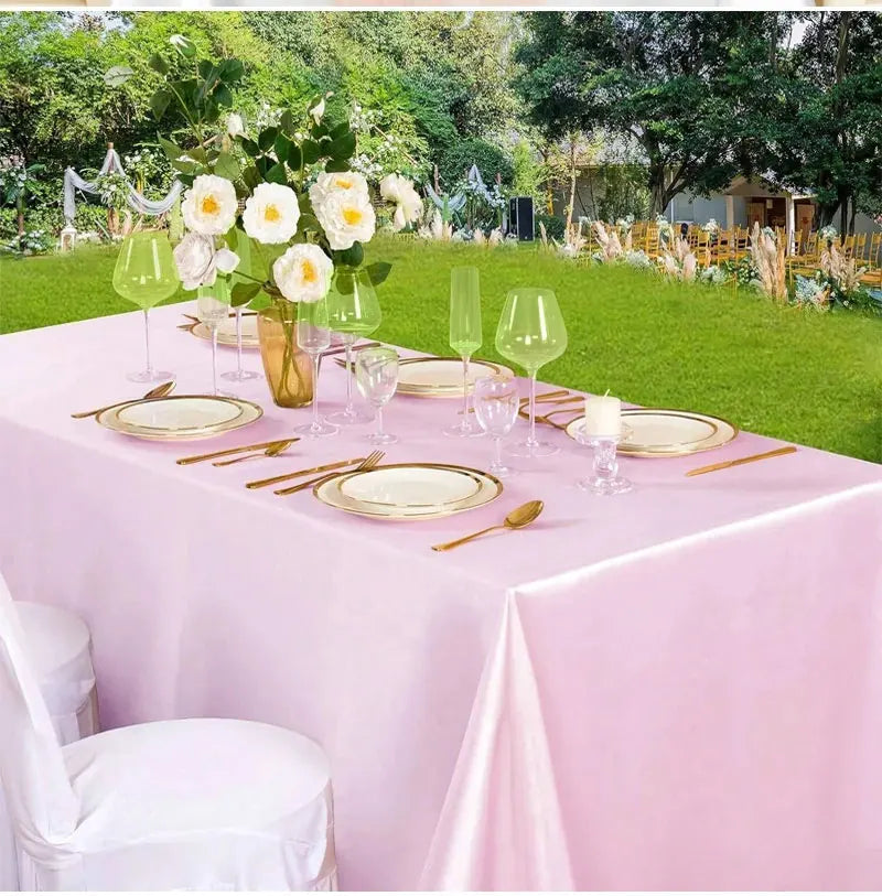 A pink satin tablecloth set for a formal outdoor dining event with floral decorations and glassware.