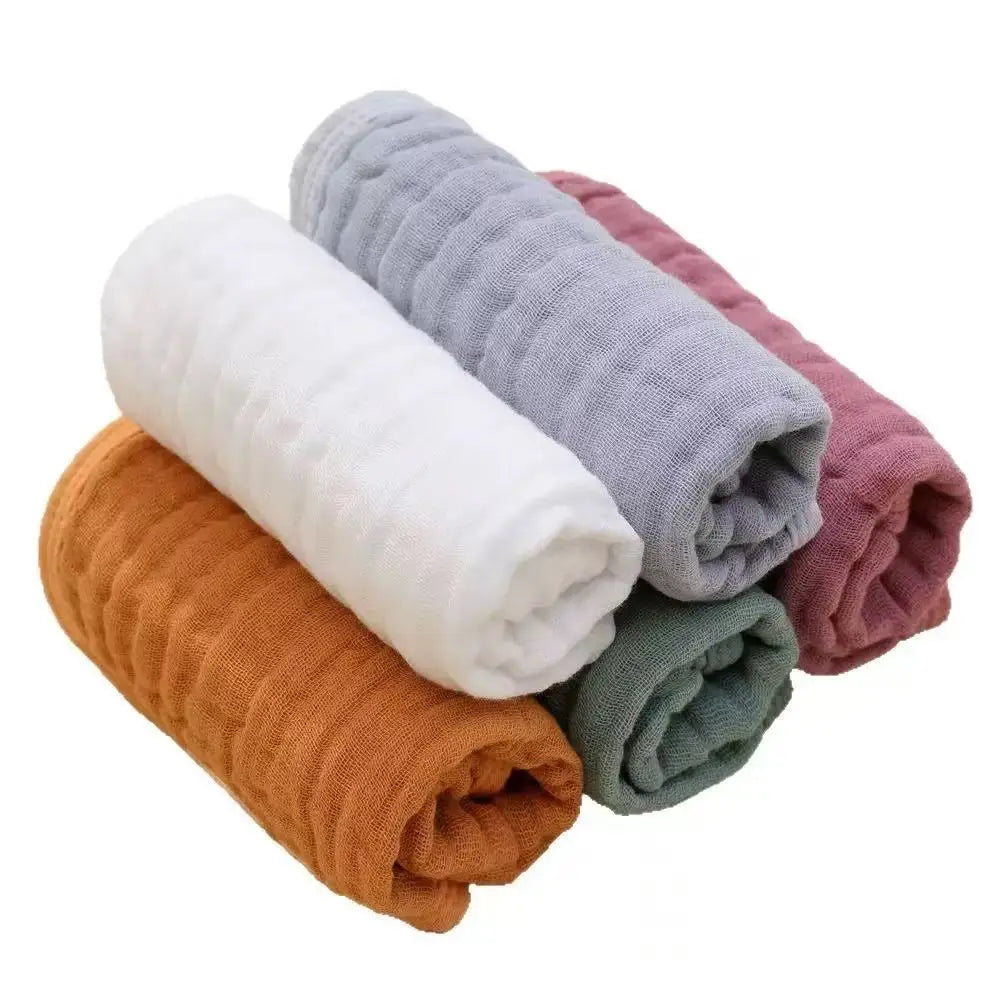 A stack of five folded cotton muslin baby burp cloths in white, gray, orange, and pink tones.