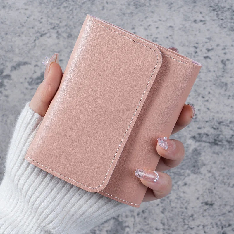 A hand holds a pink slim triple-fold PU leather wallet against a gray background.
