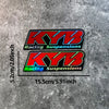 Two black and red stickers featuring the KYB Racing Suspensions logo on a gray textured background.