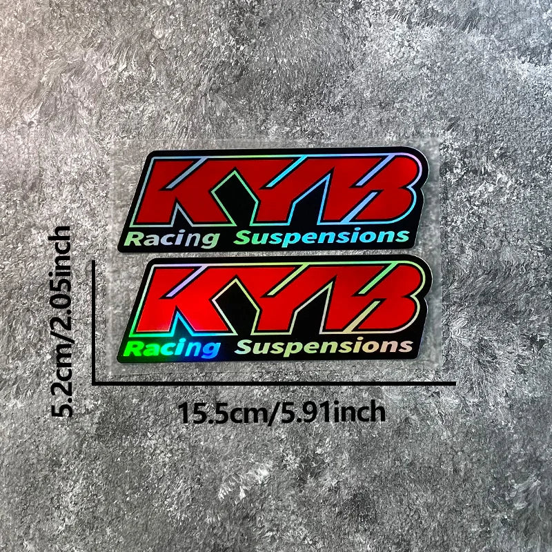 Two black and red stickers featuring the KYB Racing Suspensions logo on a gray textured background.