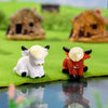 Two adorable resin Highland cow figurines, one white and one orange, displayed on green grass.