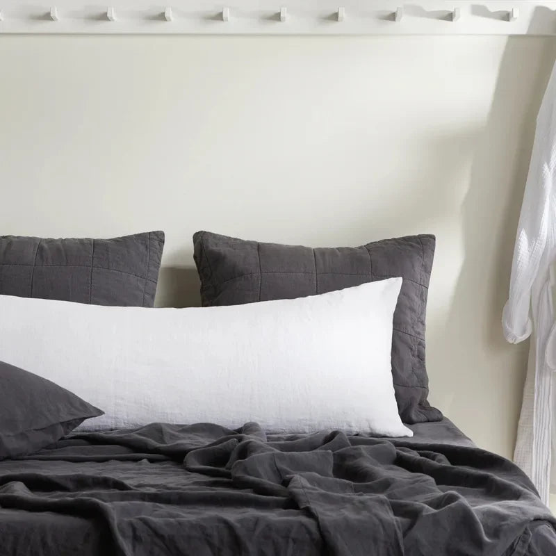 A white linen pillowcase with an envelope closure resting on a dark gray duvet in a bedroom setting.