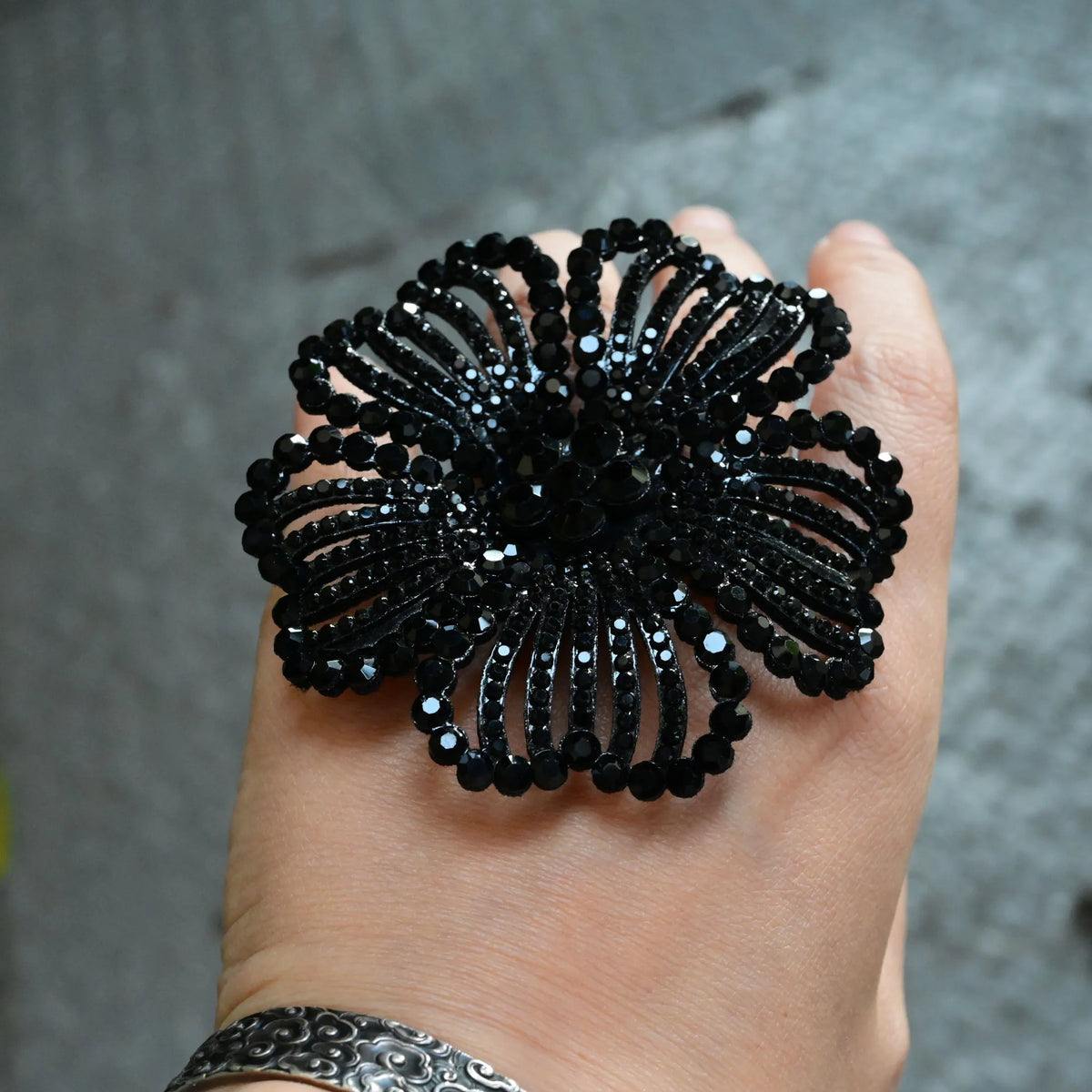 A hand holds a black crystal rhinestone flower patch with a dark, textured background.