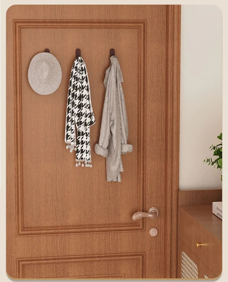 A wooden door features three hooks displaying a black and white patterned towel, a gray robe, and a round woven mat.
