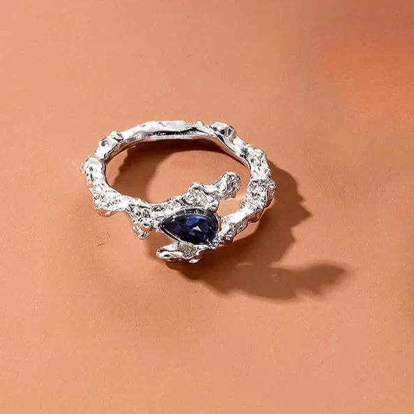 Silver irregular heart-shaped ring featuring a dark blue gemstone.