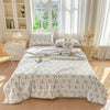 A light gray pastoral print lightweight summer quilt displayed on a bed with white and natural wood decor.