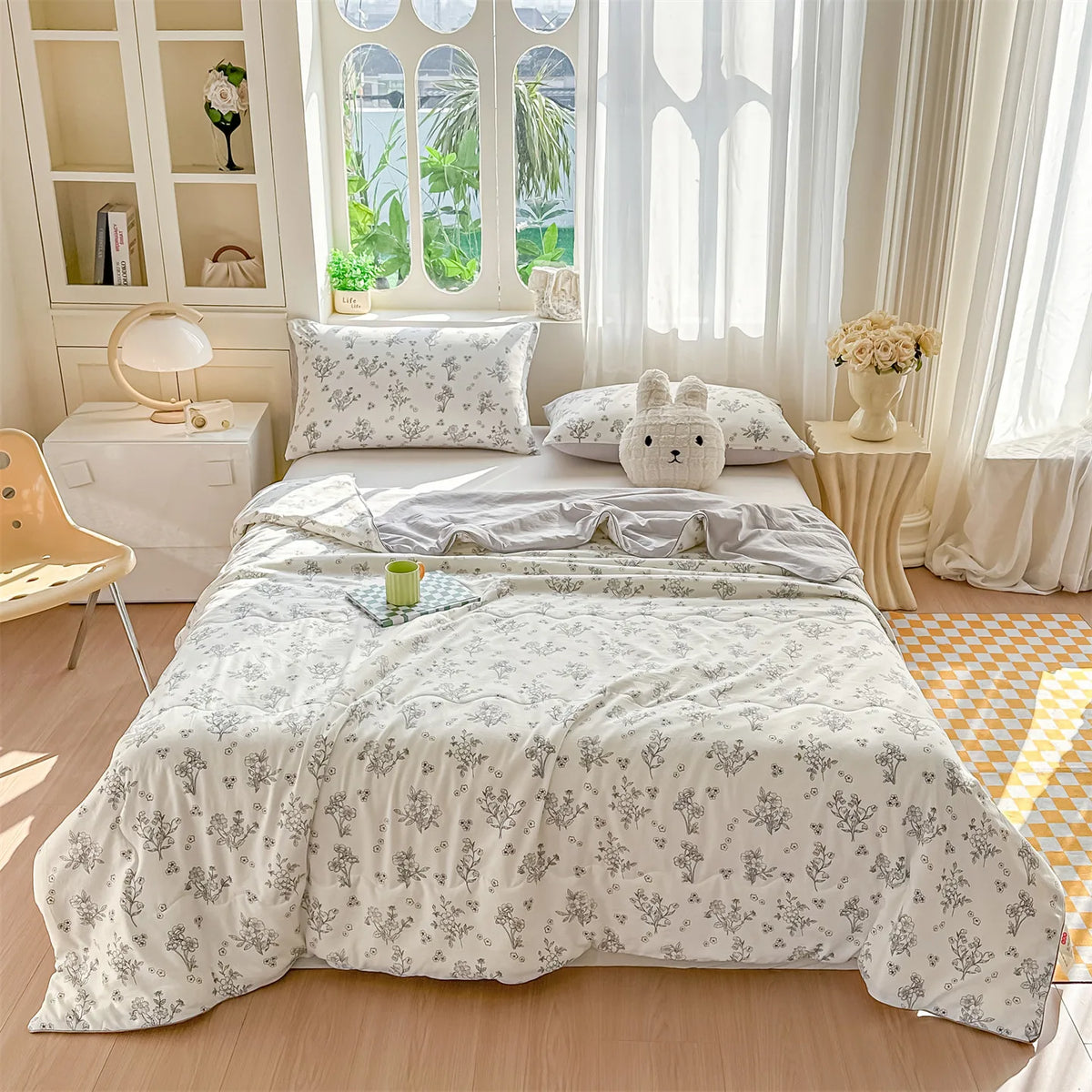 A light gray pastoral print lightweight summer quilt displayed on a bed with white and natural wood decor.