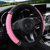 A black steering wheel with a pink quilted faux leather cover featuring diamond accents in a car interior.