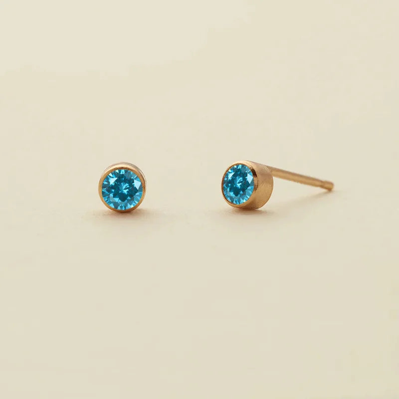 Une paire de boucles d'oreilles à clous dorés minimalistes avec des pierres bleues de naissance vibrantes.
