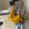 A mustard yellow lightweight nylon crossbody bag with a woven strap is worn by a person in a gray sweatshirt.