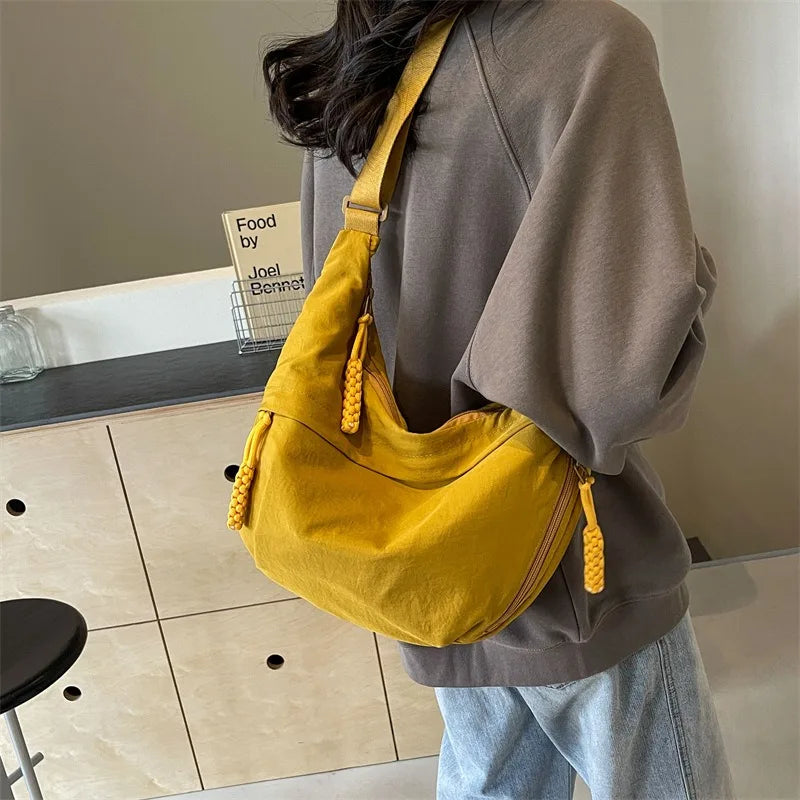 A mustard yellow lightweight nylon crossbody bag with a woven strap is worn by a person in a gray sweatshirt.