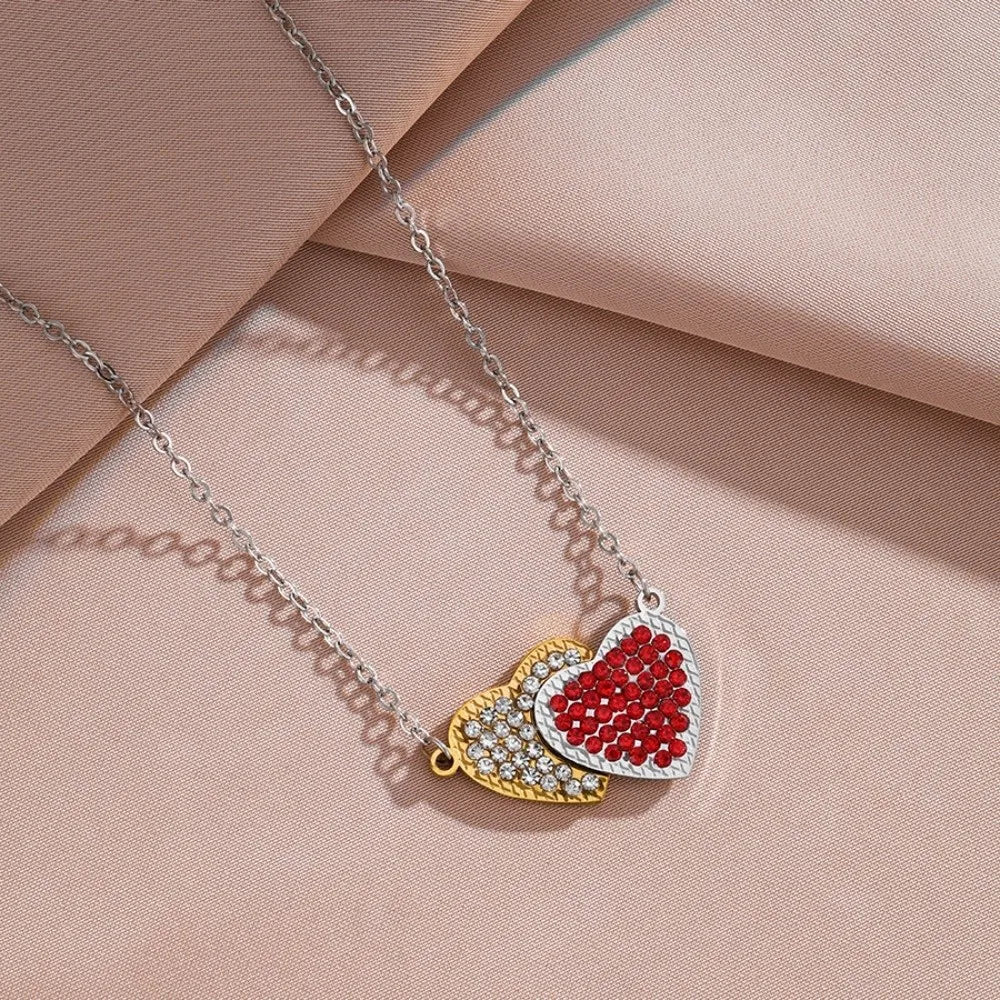 Silver chain necklace with a heart pendant featuring red and gold stones on a pink background.
