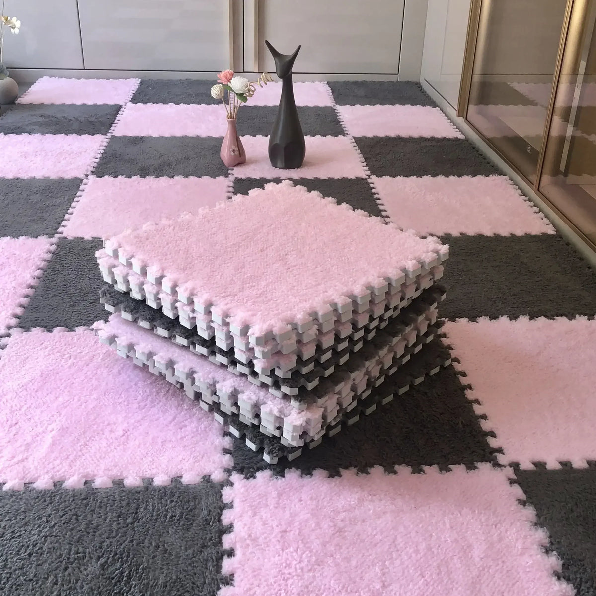Pink and gray interlocking floor tiles with a pink fluffy mat and a black decorative object.
