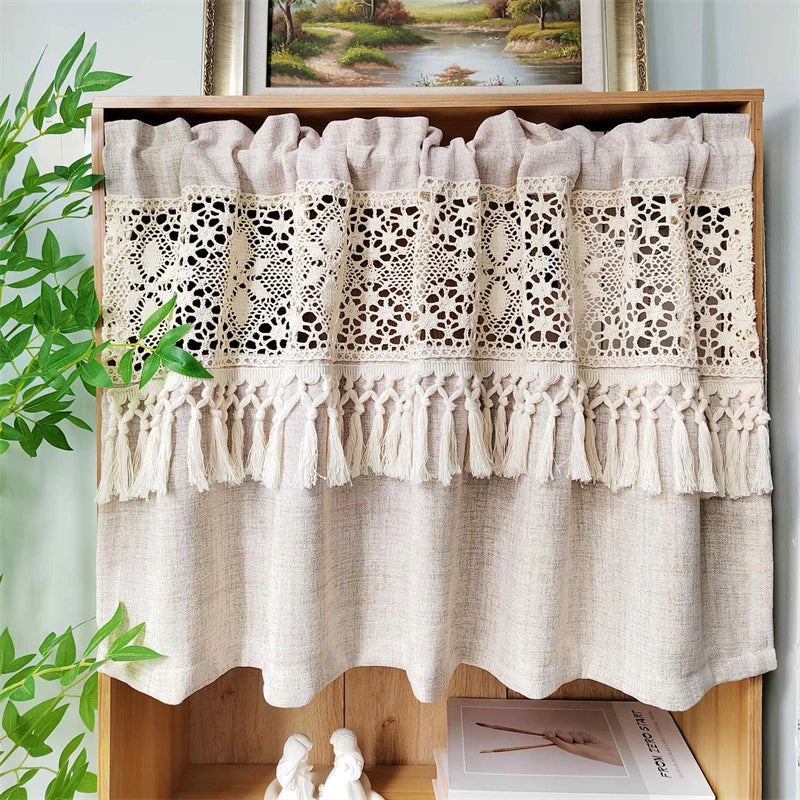 Beige sheer curtain with lace trim and tassel fringe displayed in a wooden shelf.