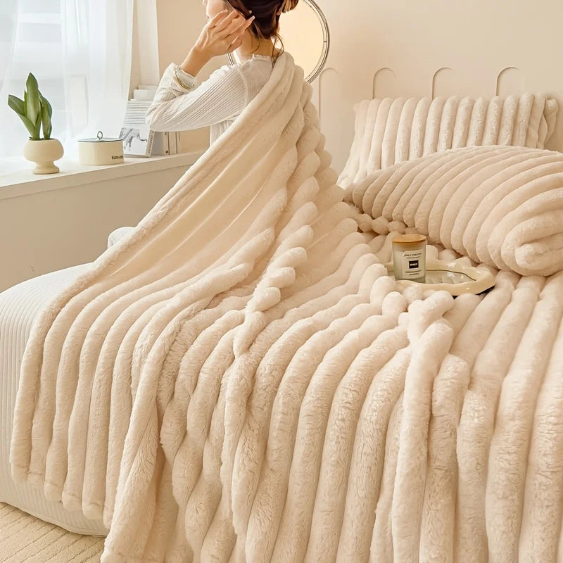 A thick, cream-colored flannel blanket draped over a bed, with a person in a white top standing near a mirror.