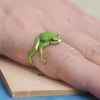 A hand wearing a small, adjustable ring shaped like a green tree frog on a finger.