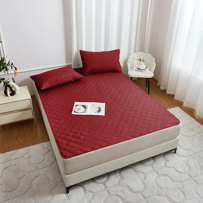 A red waterproof mattress protector with elastic straps is displayed on a bed, featuring quilted texture and soft fabric.