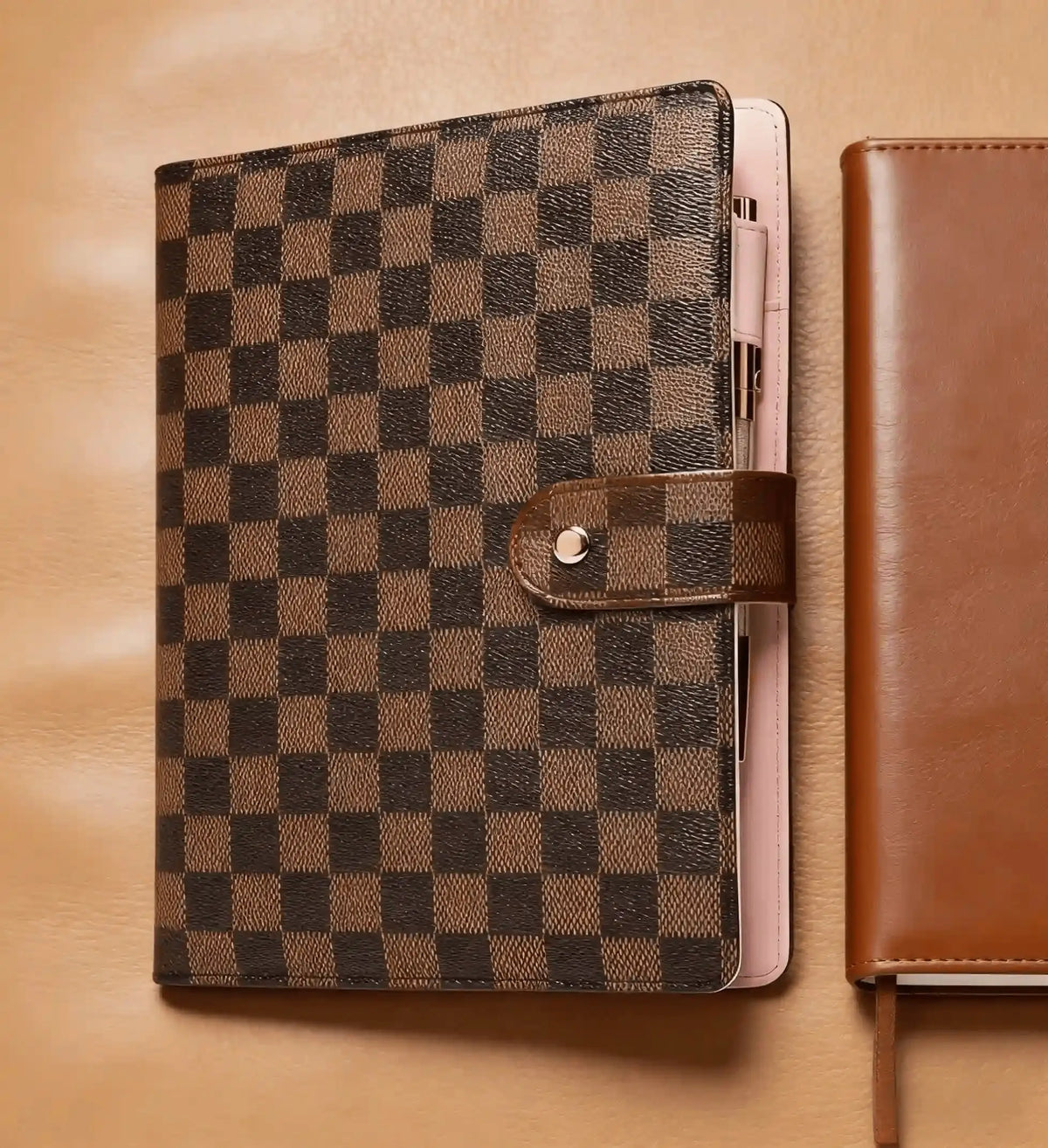 A black and brown checkered PU leather portfolio with a leather strap resting on a tan leather surface.