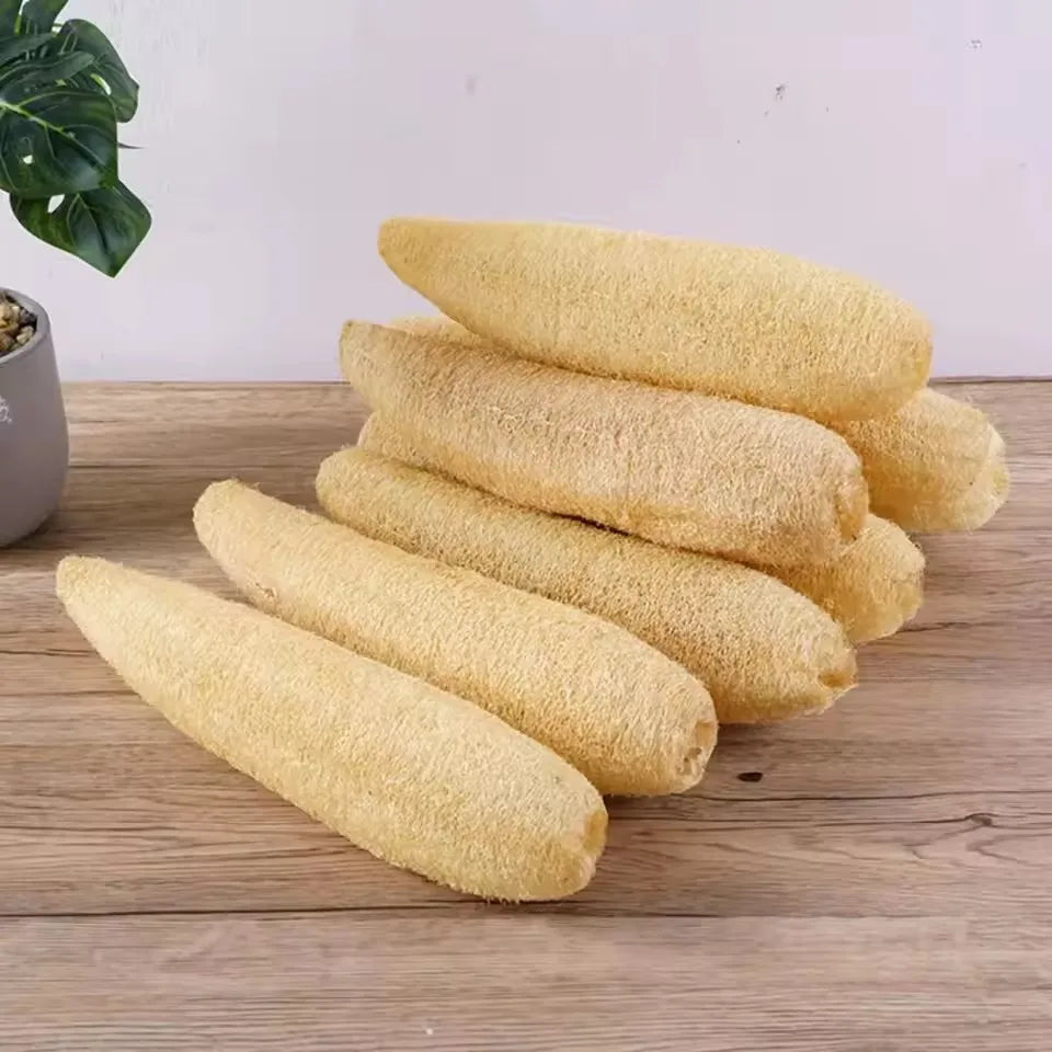 A stack of natural yellow loofah body scrubbers with hanging ropes resting on a wooden surface.