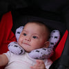 A baby is resting with a purple patterned head and neck support pillow inside a car seat.