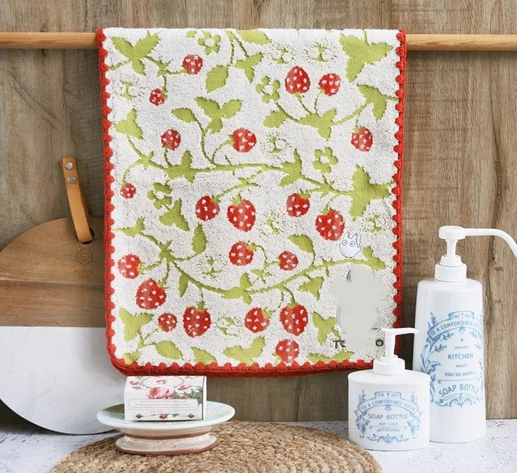A pure cotton embroidered cartoon face towel hanging on a wooden rod with soap bottles nearby.