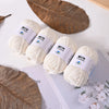 Several balls of white milk cotton yarn are displayed next to a large dried leaf on a white surface.