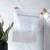A hand holds a clear mesh laundry bag with a white zipper, demonstrating the delicate wash bags.