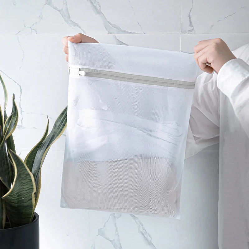 A hand holds a clear mesh laundry bag with a white zipper, demonstrating the delicate wash bags.