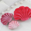 A set of three decorative velvet shell print throw pillows in shades of pink and red resting on a white surface.