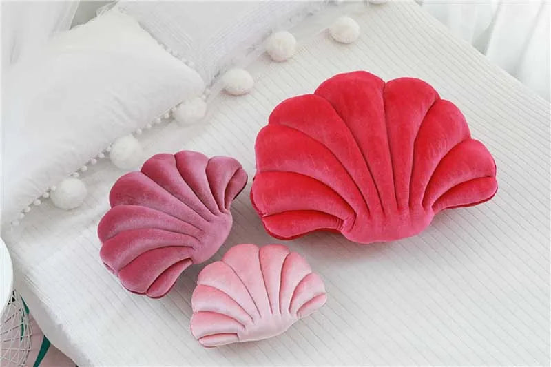 A set of three decorative velvet shell print throw pillows in shades of pink and red resting on a white surface.