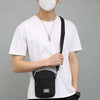 A person wearing a white t-shirt and black cap holds a black mini crossbody phone bag with an adjustable strap.