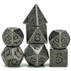 A set of seven metal polyhedral dice with a dragon font design stacked and scattered on a white background.
