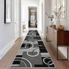 A long runner rug with a geometric pattern in black, grey, and white is placed on a light wood floor in a modern hallway.