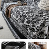 A black and white floral jacquard sofa blanket with tassels draped over a sofa.